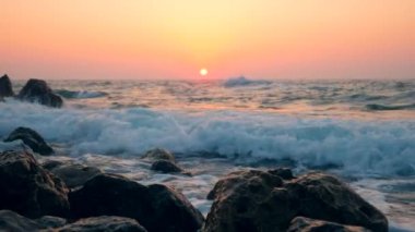 Gün batımı arka planında kayalara vuran dalgalar.