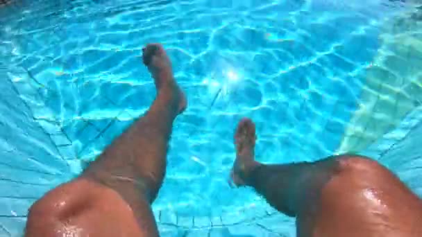 El hombre cuelga sus piernas en el agua de una piscina. Concepto vacaciones de verano . — Vídeos de Stock