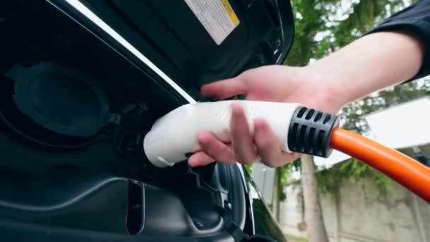 Een man neemt de oplaadkabel van een stopcontact op elektrische auto. Innovatief elektrisch hybride auto opladen. — Stockvideo