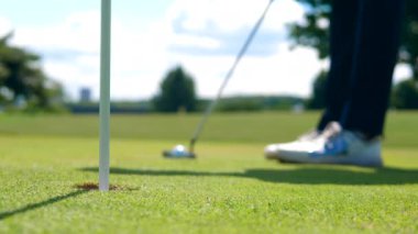 Top yuvarlanıyor ve golf deliğine düşüyor.