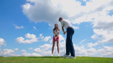 Erkek eğitmen bir kıza golf oynamayı öğretiyor.