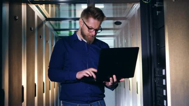 A man types on a laptop, working at a data center. IT support concept. — Stock Video