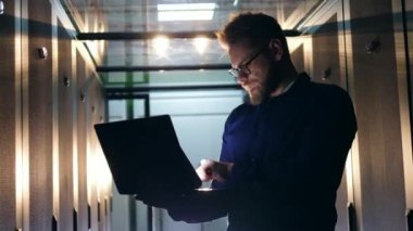 Modern veri merkezinde çalışan sunucu teknisyeni. Bir kişi bir dizüstü bilgisayar ile çalışır, bir veri merkezi odasında ayakta.