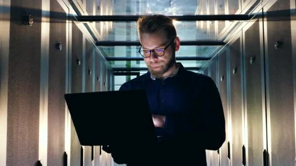 Un ingeniero trabaja con una computadora portátil, revisando las computadoras de la sala de servidores. Concepto de apoyo TI . — Vídeo de stock