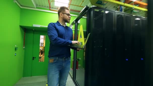 Manliga programmerare kontrollerar rack med datorer, promenader i ett serverrum. — Stockvideo