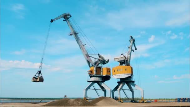 Dois guindastes de trabalho descarregam pedras em um porto . — Vídeo de Stock