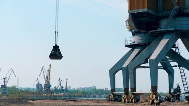 Une grue avec un seau décharge des décombres à un port sur un fond de ciel . — Video