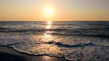 Deniz dalgaları ve gün batımı arka planda bir plaj.