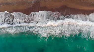 Mavi dalgalar kum kıyısına vuruyor.