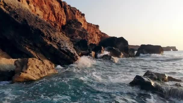 Gün batımı arka planda kayalara karşı deniz dayak. — Stok video