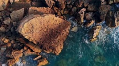 Yüksek kayalara karşı dövülen mavi bir denizin havadan görünümü.