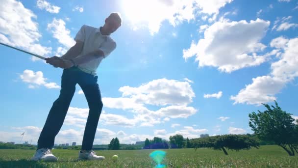 Ο νεαρός άντρας χτυπά μια μπάλα παίζοντας γκολφ σε ένα μάθημα. — Αρχείο Βίντεο