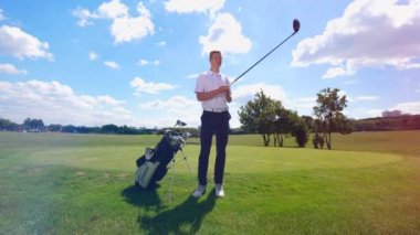 Golf oyuncusu çim sahasında metal bir kulübü test ediyor.
