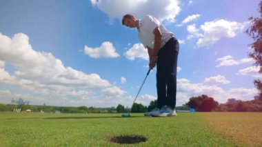 Profesyonel golfçü bir çim alanında deliğe bir top vurur.