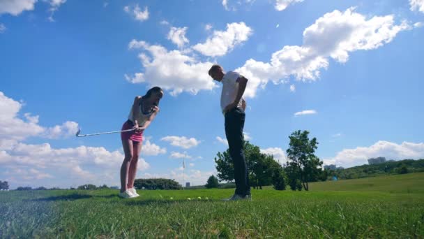 En kvinna träffar en boll medan en man tittar på ett Golf fält. — Stockvideo