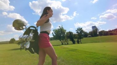 Neşeli kadın kulüpleri ile çanta tutarak, bir golf alanında yürüyor.