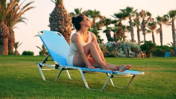 Una dama está sentada en una tumbona en una playa soleada — Vídeo de stock