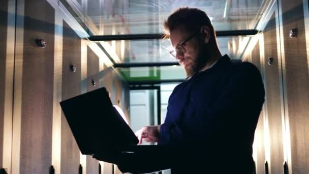 Bilgisayar sistemi güvenlik uzmanı. Bir adam bir sunucu odasında, bir dizüstü bilgisayar ile çalışan duruyor. — Stok video