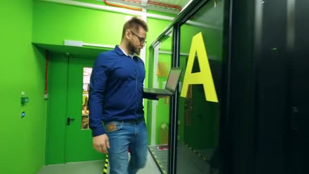 Ingeniero joven camina en una sala de servidores, mirando las computadoras . — Vídeo de stock