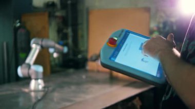 Bir kişi çalışan bir robot kolu kontrol etmek için tablet kullanır.
