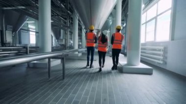 Üç teknisyen damıtma tesisi boyunca yürüyor.