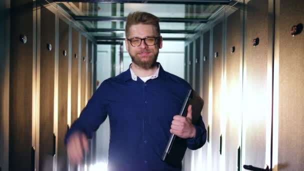 Ein lächelnder IT-Spezialist steht mit einem Laptop in einem Serverraum — Stockvideo