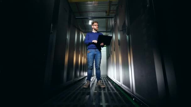 Sala de servidores escura com um engenheiro de suporte de TI olhando para as unidades — Vídeo de Stock