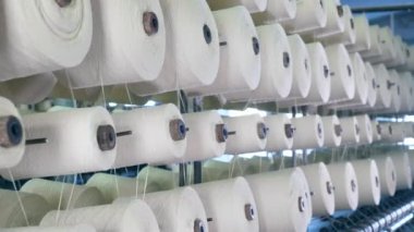 Beyaz dişli makaralar yavaşça dönüyor. Modern tekstil fabrikası.
