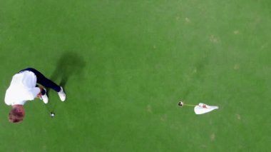 Kişi yeşil bir ders üzerinde golf oynar, deliğe bir top koyarak.