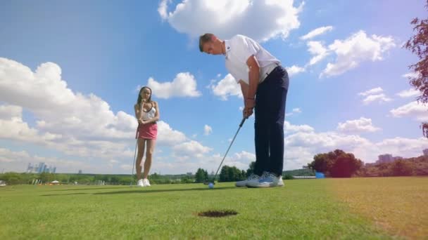 La balle tombe dans le trou avec un homme et une femme qui la regardent — Video