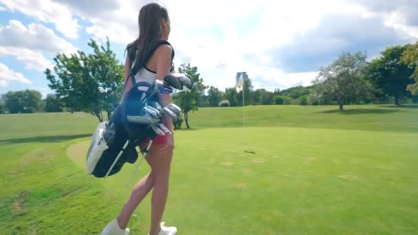 Jonge dame met golf accessoires loopt langs het gazon — Stockvideo