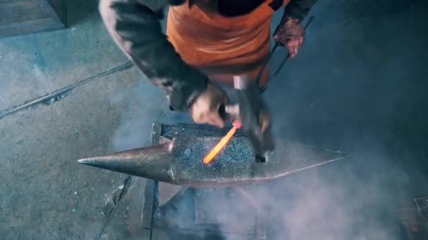 Кузнец стучит металлическим инструментом по наковальне — стоковое видео