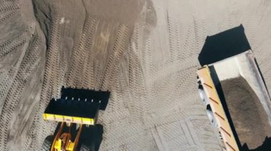 İş makinesi bir taş ocağında ezilmiş taşlarla bir kamyon yükler.