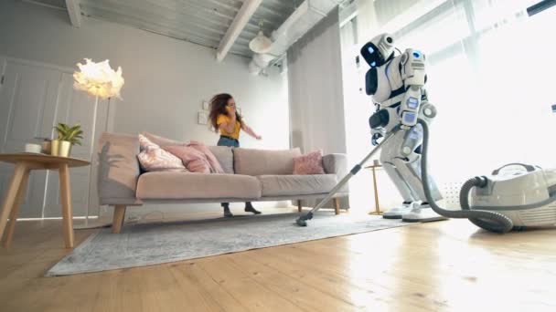 Το ανθρώπινο ρομπότ καθαρίζει το δωμάτιο με μια γυναίκα που κάθεται στον καναπέ. — Αρχείο Βίντεο
