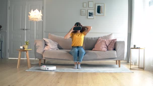 Une dame met des lunettes VR dans la pièce avec un aspirateur robotisé — Video