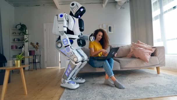 Young woman is operating a laptop and consulting a cyborg — Stock Video