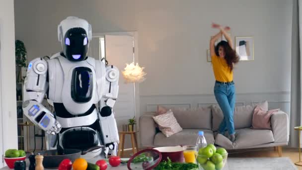 A lady is jumping on a sofa while a robot is cooking — Stock Video