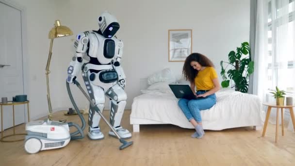 Um cyborg é hoovering e uma mulher está trabalhando em um laptop — Vídeo de Stock