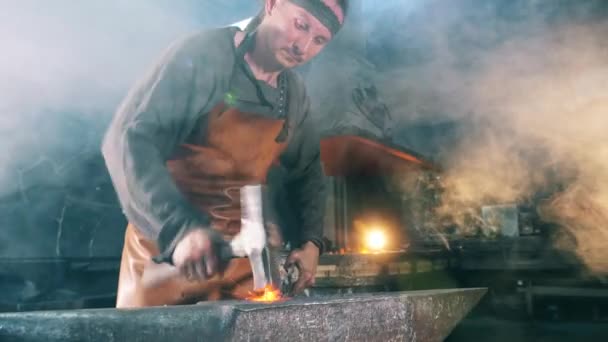 Um homem trabalha numa forja, a bater numa faca com um martelo. . — Vídeo de Stock