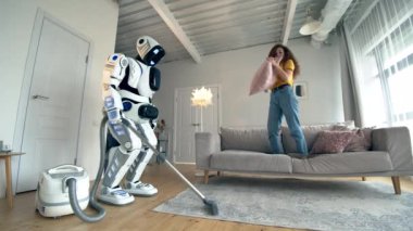 Beyaz Robot Vakum temizlik yaparken genç kadın yastıklar ile oynuyor.
