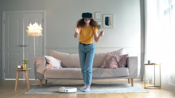 Ragazza utilizza VR auricolare mentre un aspirapolvere robotico funziona . — Video Stock