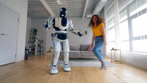 Um robô dança enquanto uma mulher salta para uma sala. Ciborgue e conceito humano . — Vídeo de Stock