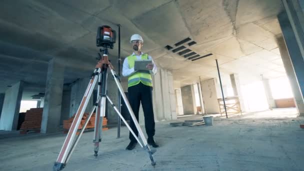 Architect with tablet uses a walkie talkie, standing in the unfinished building. — Stock Video