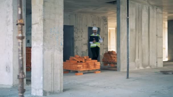 Constructor, ingeniero con un portátil camina en un edificio, de cerca . — Vídeos de Stock