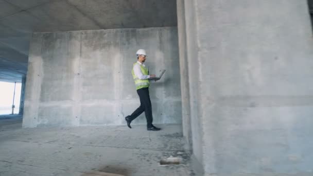 Μηχανικός, αρχιτέκτονας περπατάει κρατώντας ένα φορητό υπολογιστή, πλευρική θέα. — Αρχείο Βίντεο