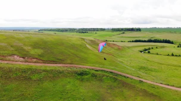 Gröna fält och en person som gör skärmflygning längs dem. Extreme Sport Concept. — Stockvideo