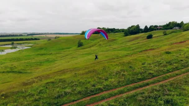 Зеленые поля с человеком, бегущим и летающим на парашюте — стоковое видео