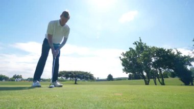 Bir adam sahada golf oynuyor, topa vuruyor..