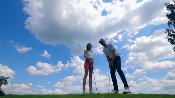 Hombre enseña a una mujer a jugar al golf en un campo . — Vídeos de Stock