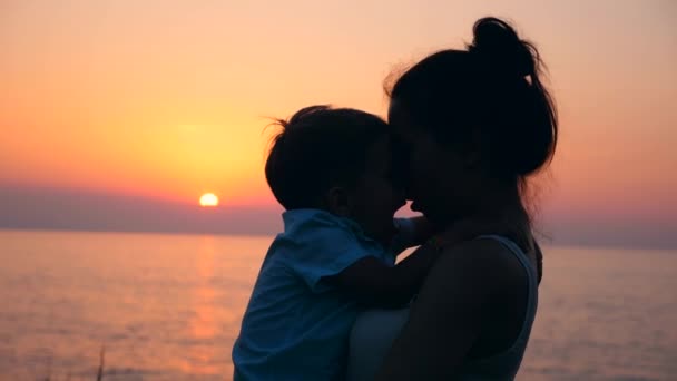 Ein Kind und seine Mutter umarmen und küssen sich bei Sonnenuntergang. Mutter und Baby, Mutterschaftskonzept. — Stockvideo